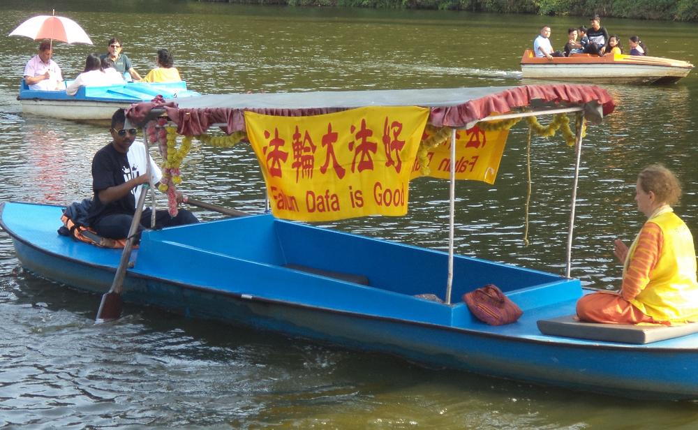 Praktikantica na čamcu sa transparentom na kojem piše „Falun Dafa je dobar”.