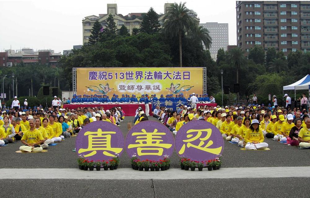 Masovne grupne vježbe. Na transparentu u pozadini stoji: „Proslava 13.5. Svjetskog Falun Dafa dana“. Kineski znakovi ispred praktikanata znače: „Istinitost-Dobrodušnost-Tolerancija“.
