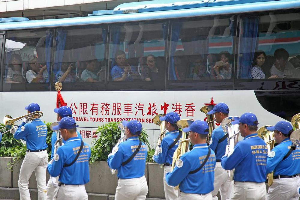 Kineski turisti u autobusu slikaju dok Divine Land Marching Band prolazi pored njih.
