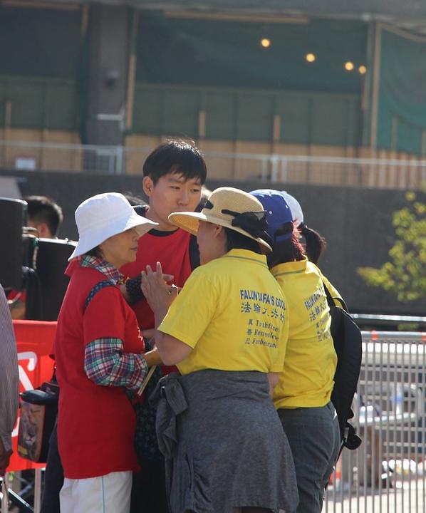 Dva praktikanta (u žutoj odjeći) objašnjavaju kineskim posmatračima (u crvenom) Falun Gong i progon u Kini. 