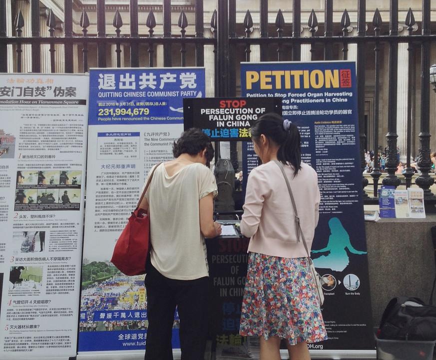 Turisti proučavaju plakate koje su izložili praktikanti i uče o Falun Gongu.