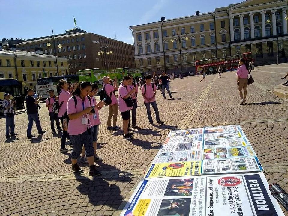 Grupa kineskih turista čita postere o Falun Gongu na trgu Senata 