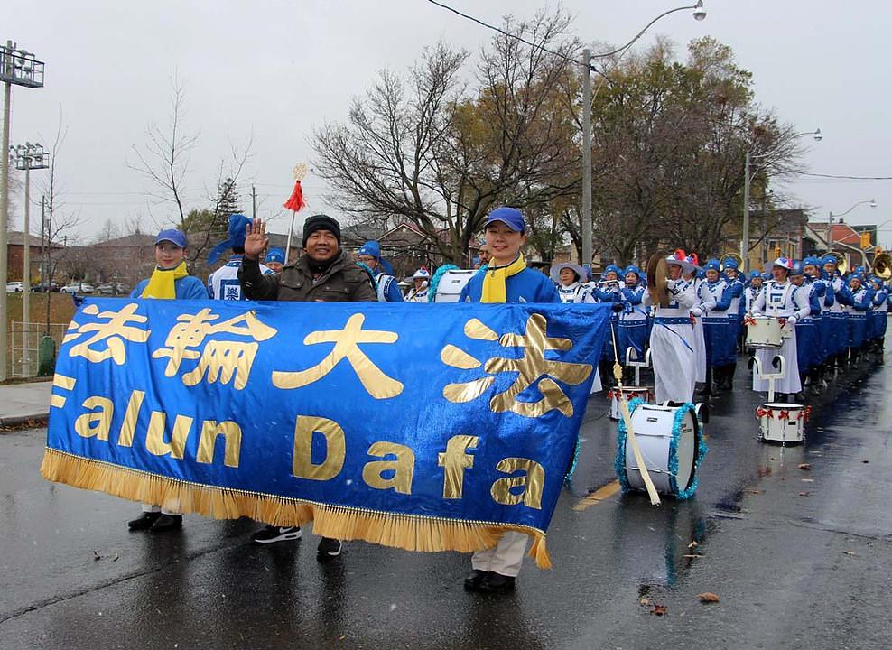 Rowel, koji je ove godine u Kanadu imigrirao sa Filipina, stoji sa praktikantima i drži transparent. Zamolio je svoju suprugu Lyn da napravi fotografije. Ovom se paru orkestar veoma dopao, a još su kazali da će na internetu potražiti više informacija o Falun Gongu.