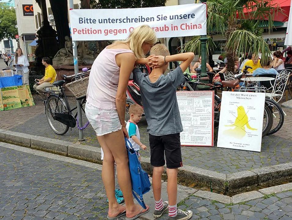 Majka i sin čitaju oglasnu ploču o zločinima prisilne žetve organa u Kini koja se vrši u organizaciji države.