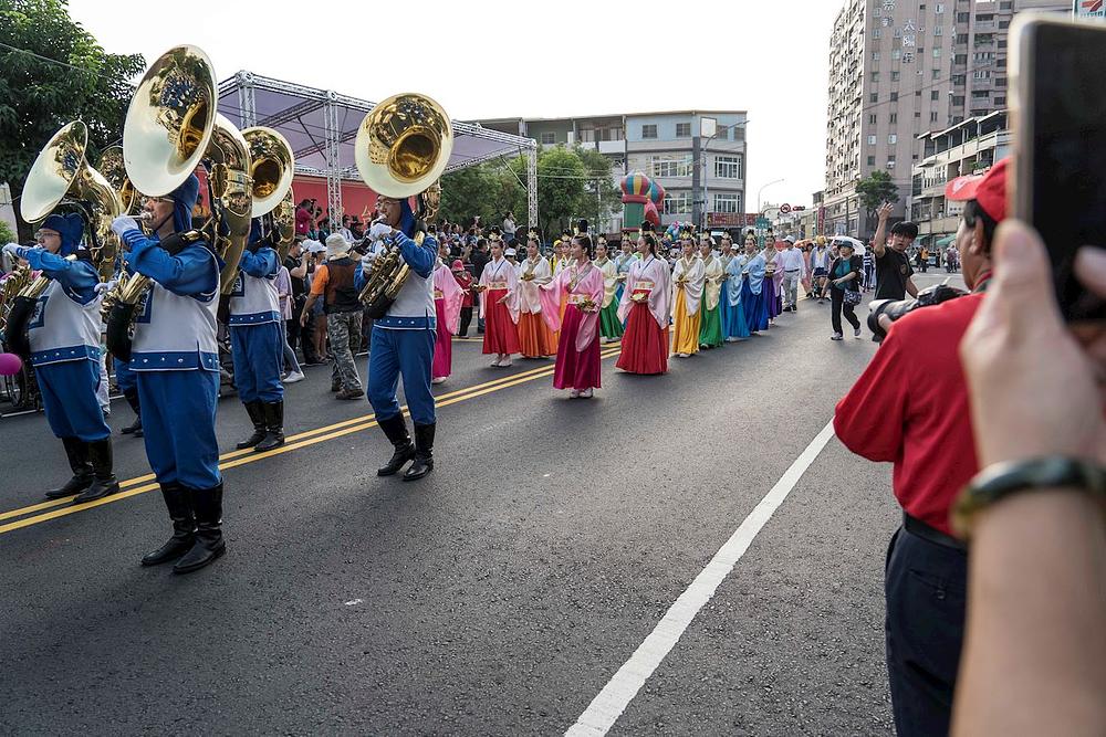 Praktikantice u odjeći "nebeskih djevojaka" drže velike cvjetove lotosa i slijede Tian Guo Marching Band.
 
